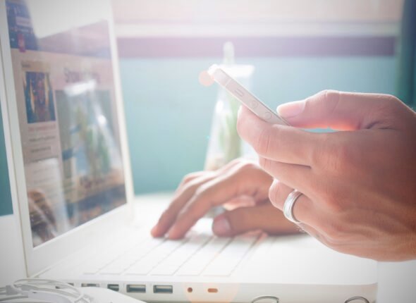 Man's hand holding smartphone and using laptop for online marketing